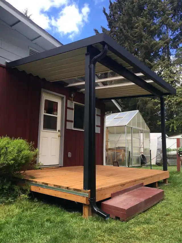 Black aluminum frame cover with cream roof panels over a cedar deck, a downspout running down one post