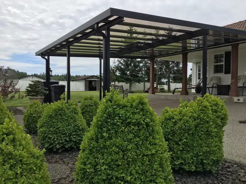 Dark open-frame cover on a posted patio behind clipped shrubs