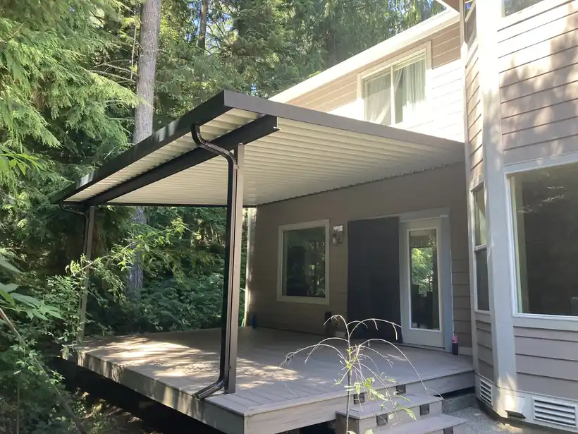 Dark aluminum patio cover over a deck among tall firs
