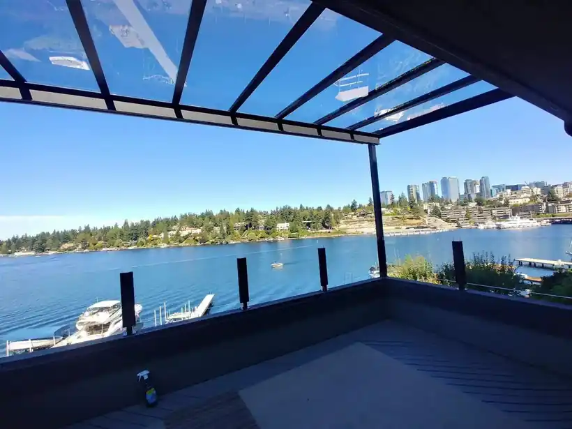 Clear glass patio cover on black aluminum beams over a waterfront rooftop deck