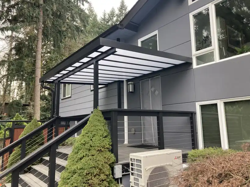 Dark pergola-style cover along the side of a grey house