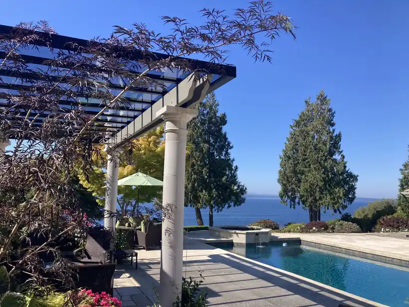 Timber and white pergola cover beside a pool with a water view