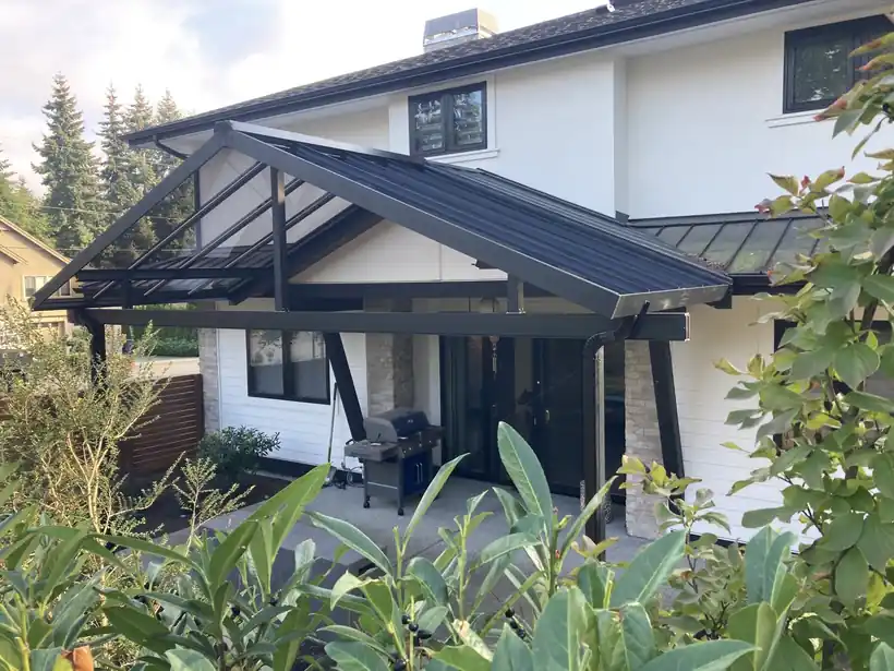 Dark pitched patio cover over a patio behind a white two-storey house